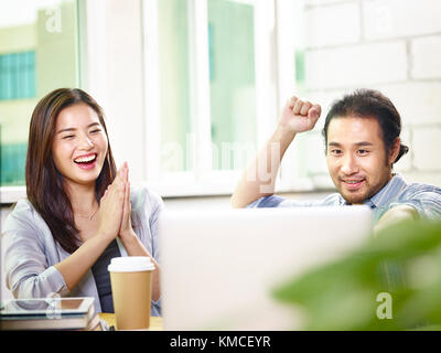 Deux jeunes entrepreneurs asiatiques looking at laptop computer célébrant les succès et les réalisations dans le bureau. Banque D'Images