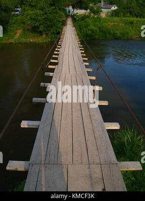 Pont sur la rivière : un passage en bois sur une petite rivière, dans la végétation verte abondante de distance. Banque D'Images