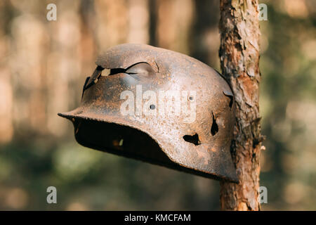 Endommagés par les balles et les éclats casque de métal de l'infanterie allemande soldat de la Wehrmacht lors de la Seconde Guerre mondiale. Casque rouillé accroché sur tronc d'arbre. Banque D'Images