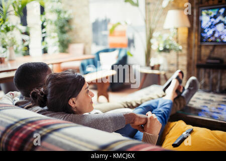 Un jeune couple affectueux regardant la télévision sur le canapé du salon Banque D'Images