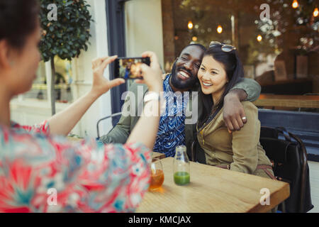 Femme photographiant affectueuse couple amis avec appareil photo téléphone au trottoir café Banque D'Images