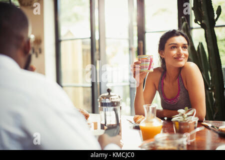 Femme souriante buvant du café à la table du petit déjeuner Banque D'Images