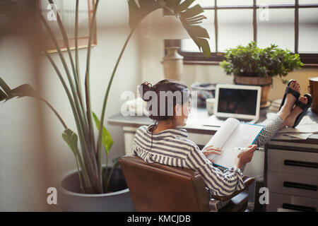 Femme d'affaires lisant les documents avec les pieds sur le bureau Banque D'Images