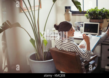 Femme d'affaires lisant les documents avec les pieds sur le bureau Banque D'Images