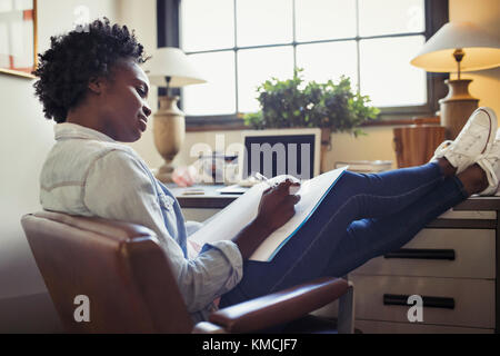 Femme d'affaires examinant les documents avec les pieds vers le haut sur le bureau Banque D'Images