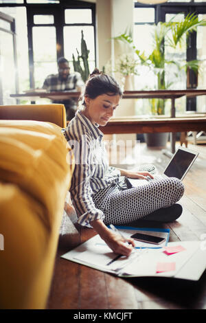 Femme indépendante travaillant à l'ordinateur portable, prenant des notes au niveau du salon Banque D'Images