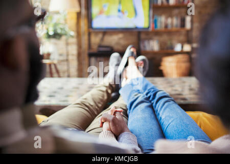 Couple affectueux tenant les mains, regardant la télévision dans le salon Banque D'Images