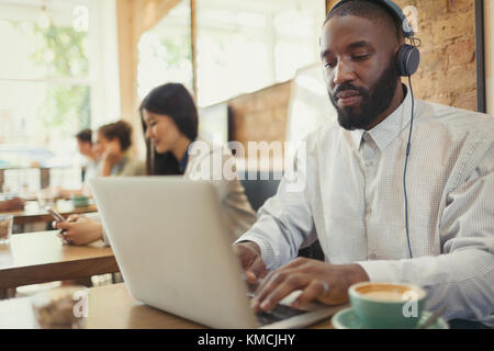 Jeune homme avec un casque utilisant un ordinateur portable et de boire du café à table basse Banque D'Images