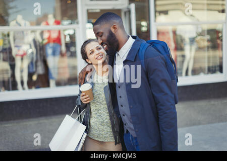 Jeune couple affectueux avec un café et un sac à provisions à l'extérieur de la boutique Banque D'Images