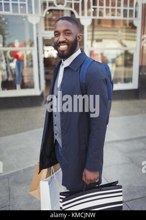 Portrait jeune homme souriant et confiant avec des sacs à provisions à l'extérieur de la vitrine Banque D'Images