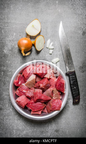 Des morceaux de viande dans un bol avec un couteau à découper et un oignon. sur la table de pierre. Vue de dessus Banque D'Images