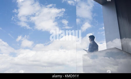 Homme d'affaires pensif debout sur un balcon moderne avec vue sur le ciel bleu et les nuages Banque D'Images
