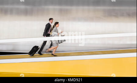 Homme d'affaires et femme d'affaires avec une valise qui monte sur la rampe d'accès à l'aéroport Banque D'Images