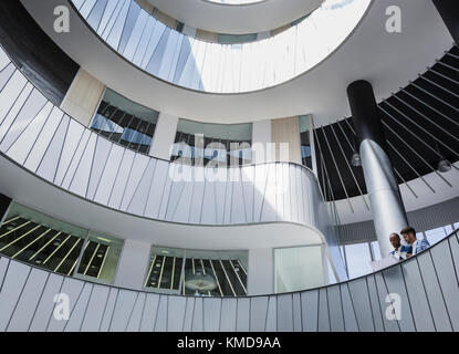 Les hommes d'affaires discutent de la paperasse sur le balcon de l'atrium de bureau moderne et architectural Banque D'Images