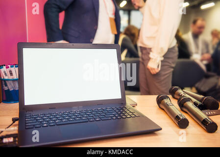 Close up portable avec écran vide et micros sur la table dans la salle de conférence pendant l'événement. participants floue sur l'arrière-plan d'affaires, concept. Banque D'Images