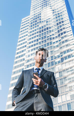 Portrait d'un homme d'affaires qui se trouve en face d'un gratte-ciel et les poignées d'un téléphone cellulaire Banque D'Images