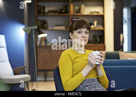 Caucasian businesswoman dans un bureau contemporain ayant une pause café avec un air pensif, contemplant Banque D'Images