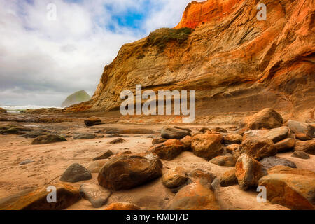 De gros rochers tombés de la falaise de grès à cape kiwanda, jonchent la plage de sable fin. Les nuages le ciel que l'on regarde en direction de rock pile foin Banque D'Images