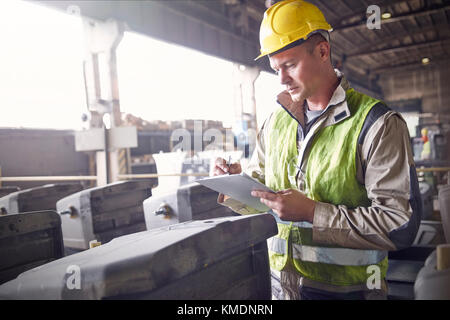 Steelworker écrit sur le presse-papiers dans l'aciérie Banque D'Images