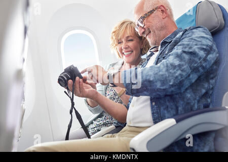 Couple d'âge mûr regardant des photos sur un appareil photo numérique dans un avion Banque D'Images