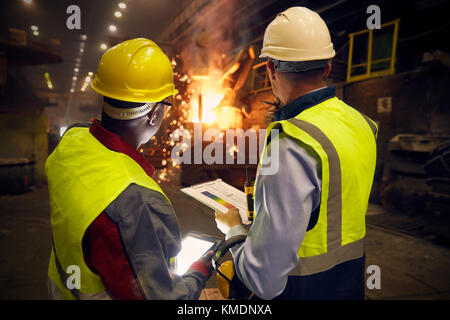 Steelworkers avec tablette numérique et presse-papiers parlant dans l'aciérie Banque D'Images