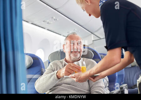 Préposé de vol servant du jus d'orange à l'homme à bord de l'avion Banque D'Images