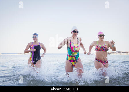 Les nageurs en eau libre féminin en marche et de s'éclabousser dans océan surf Banque D'Images