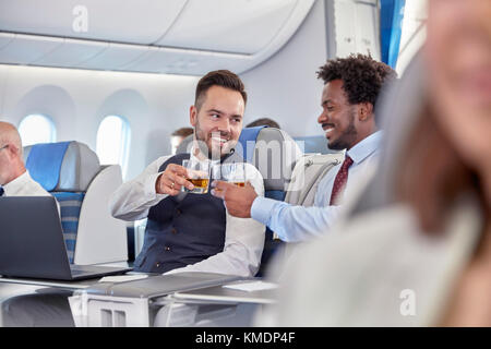 Les hommes d'affaires toasting whiskey lunettes de première classe dans un avion Banque D'Images