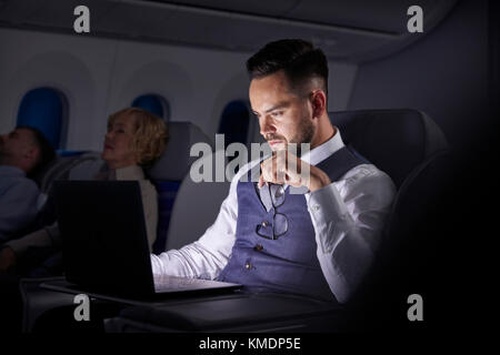 Homme d'affaires sérieux travaillant à un ordinateur portable dans un avion de nuit Banque D'Images