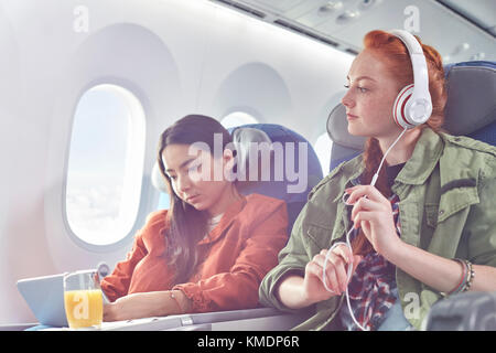 Les jeunes femmes amis avec écouteurs et digital tablet on airplane Banque D'Images