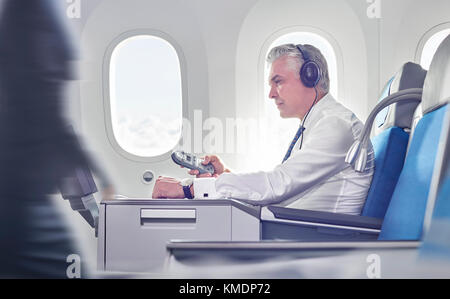 Homme d'affaires avec casque et télécommande pour regarder des films en avion Banque D'Images