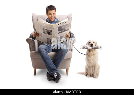 Jeune homme assis dans un fauteuil lisant un journal et un labrador retriever avec un journal isolé sur fond blanc Banque D'Images