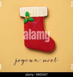 Un coloroful cookie dans la forme d'un bas de Noël et le texte joyeux Noel, joyeux Noël en français, sur un fond orange Banque D'Images