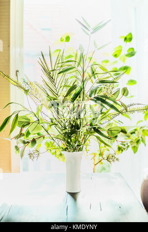 Jolies plantes bouquet dans un vase sur la table à l'arrière-plan de la fenêtre. arrangements fleuriste avec variété de plantes tropicales vert.Maison et Intérieur, backlig Banque D'Images