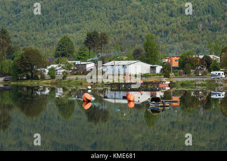 Bateaux et bâtiments réfléchi sur les eaux calmes d'un loch de mer à Puyuhuapi, une petite ville sur la Carretera Austral dans le nord de la Patagonie, au Chili. Banque D'Images