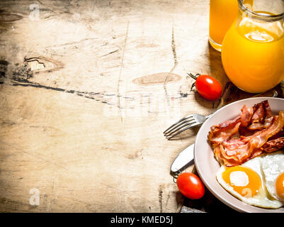 Petit-déjeuner frais. Le jus d'orange avec les œufs, le bacon et les tranches de pain. sur une table en bois. Banque D'Images