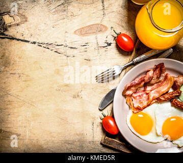 Petit-déjeuner frais. Le jus d'orange avec les œufs, le bacon et les tranches de pain. sur une table en bois. Banque D'Images