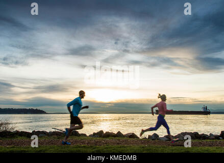 Deux coureurs silhouetté contre un ciel coloré le long des bords de la Puget Sound à Seattle, WA. Banque D'Images