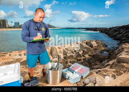 Wataru Kumagai, de la Direction de l'eau propre du Département de la santé de l'État d'Hawaï, démontre l'échantillonnage d'eau des plages hawaïennes à la plage d'Ala Moana à Honolulu à l'aide d'instruments tels qu'un turbidimètre. Pour la portée complète des lectures, des travaux de laboratoire ont été effectués hors site. Banque D'Images