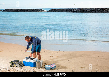 Wataru Kumagai, de la Direction de l'eau propre du Département de la santé de l'État d'Hawaï, démontre l'échantillonnage d'eau des plages hawaïennes à la plage d'Ala Moana à Honolulu à l'aide d'instruments tels qu'un turbidimètre. Pour la portée complète des lectures, des travaux de laboratoire ont été effectués hors site. Banque D'Images