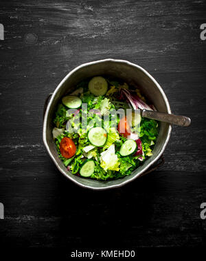 Salade de concombres et tomates avec des greens dans un vieux pot. sur la table en bois noir. Banque D'Images