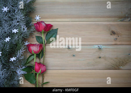 Noël romantique photographie image avec arbre vert garland saupoudré de flocons de neige et de pétales de fleurs rose et rouge sur fond de bois rustique Banque D'Images