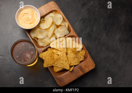 Bière en verres sur la table en béton.La bière et les en-cas sont des frites et des nachos dans un bol en bois avec une pâte au fromage. Vue de dessus.Copier l'espace.Buvez et Banque D'Images
