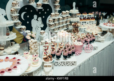 Plan de profil de la barre de chocolat de mariage couverts avec différents de délicieux desserts tels que les gâteaux, bonbons, mararons et autres sucreries en rose et blanc. l'heartwith couple dans l'amour décore la table. Banque D'Images