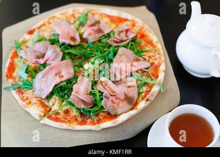 Pizza avec rôti de bœuf et salade de roquette sur une table. Banque D'Images