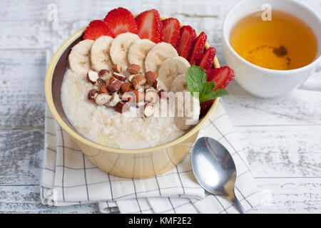 Bol de flocons d'avoine avec une banane, des fraises, des amandes, des noisettes et du beurre sur une table rustique.Un plat chaud et sain pour le petit déjeuner, vue du dessus. Banque D'Images