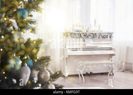 Décoration nouvel an. arbre de Noël près de piano blanc à l'arrière-plan de la fenêtre. lumière effet bokeh doux. Banque D'Images