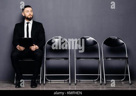 Certain demandeur d'emploi se lit reprendre alors qu'il était assis sur une chaise dans la rangée dans Office et d'attendre son tour sur l'interview. jeune homme portant costume se prépare pour re Banque D'Images