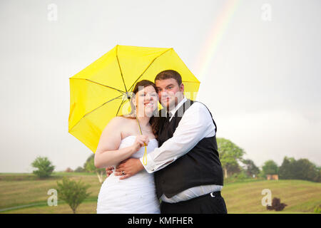 Un arc-en-ciel derrière un couple nouvellement marié sur un jour nuageux sous un parapluie Banque D'Images