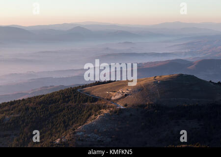 Belle vue aérienne de la montagne Subasio (Assise, Ombrie) au coucher du soleil, avec de longues ombres et couleurs chaudes, et une mer de brume remplissant la vallée ci-dessous Banque D'Images